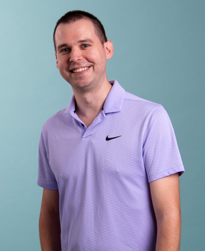 A man with short dark hair smiles while standing against a light blue background. He is wearing a light purple collared Nike shirt with short sleeves, looking ready to discuss pluq ev free loading stations.