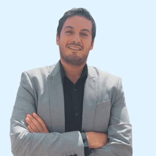 A man in a light gray suit jacket and black shirt stands with arms crossed, smiling confidently against a plain light blue background, embodying the ease and assurance of reliable charging.