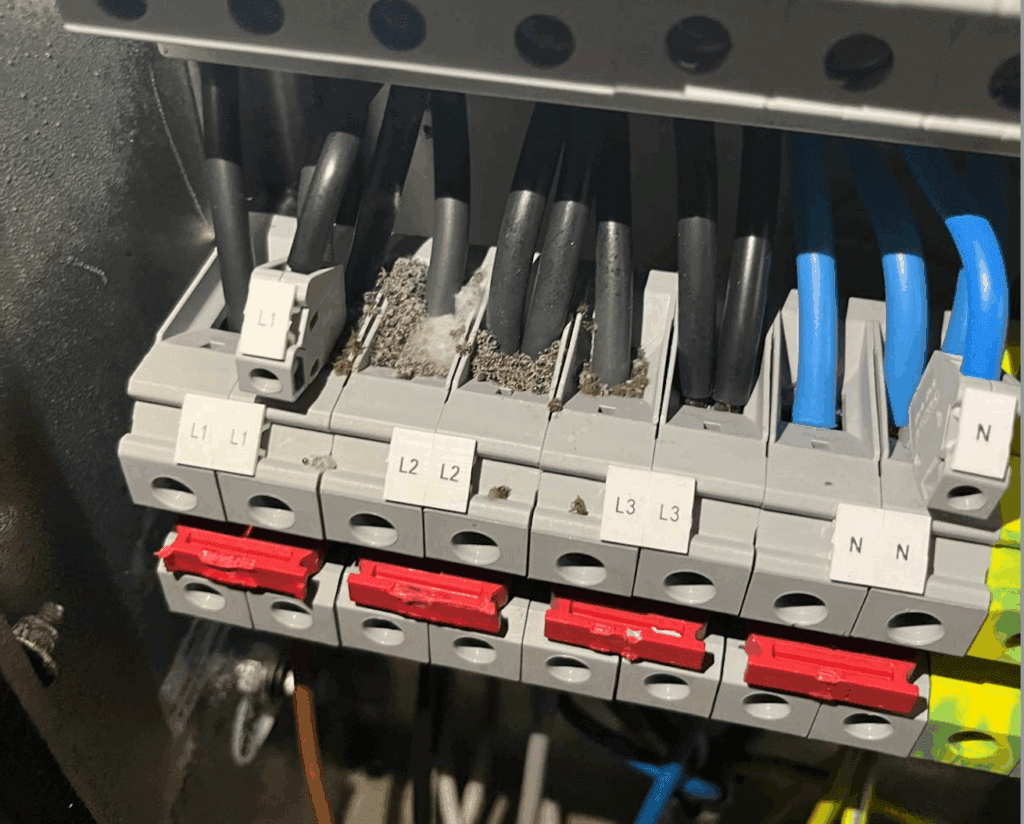 Close-up of electrical terminal blocks with labeled wires (L1, L2, L3, N). Some terminals show signs of dust or debris accumulation between the black wires and connectors. Red switches are visible below the terminals.