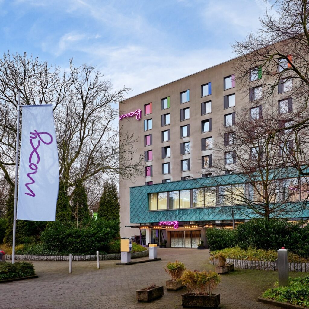 Exterior of Moxy Hotel Germany with branded flags and colorful facade, EV charging partner of Pluq